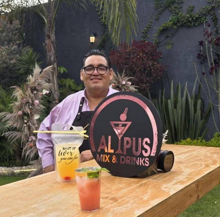 Bartender de ALYPUS en un jardín con cocteles servidos junto al letrero de la marca