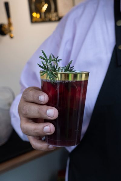 Cóctel rojo con romero en vaso de borde dorado